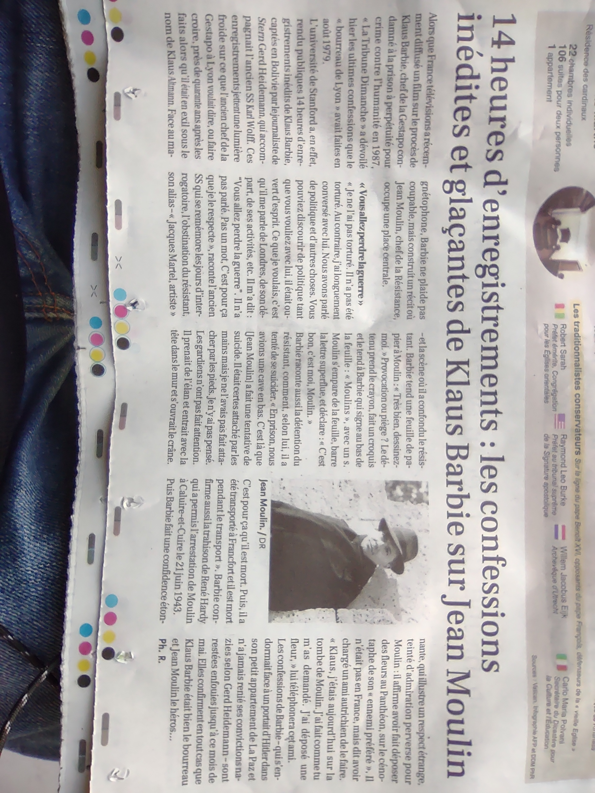 Une image prise au smartphone d'un article qui occupe le tiers bas d'un journal en papier. Le titre: "14 heures d'enregistrements : les confessions inedites et glacantes de Klaus Barbie sur Jean Moulin". L'article est aussi accompagné d'un portrait photo de Jean Moulin en noir et blanc, présumément avant sa mort dans les années 1930 ou 40.