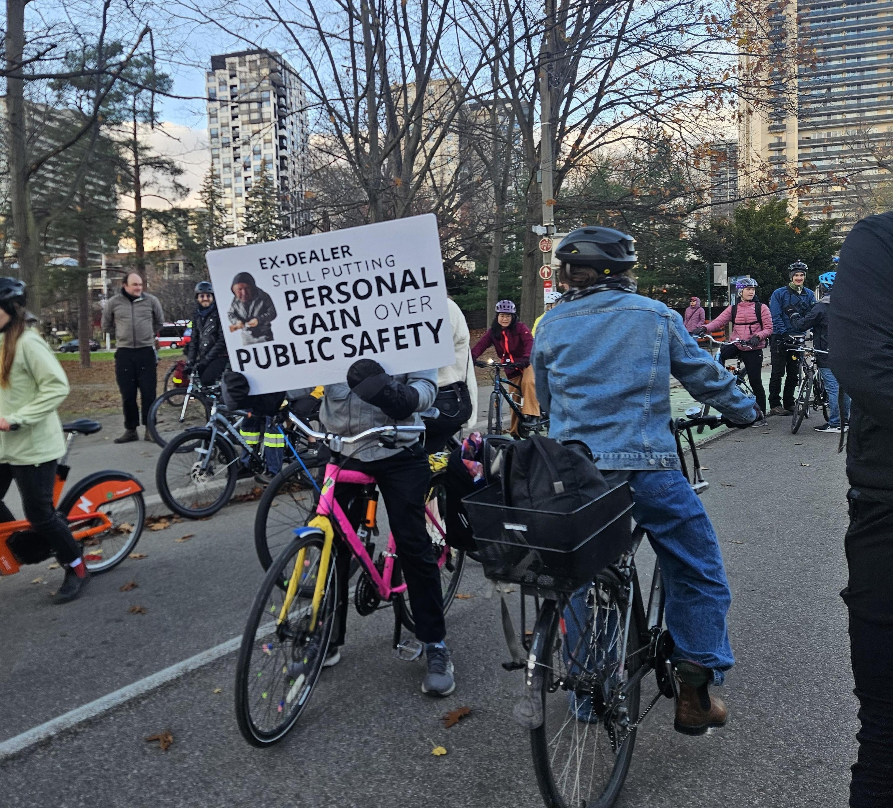 Photo of a person on a bicycle with a sign that reads "Ex-dealer still putting personal gain over public safety" with a photo of Doug Ford.